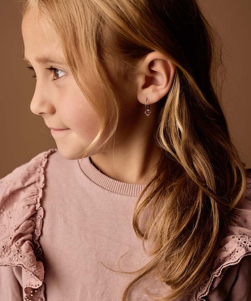 Side view af en ung pige med langt, bølget blondt hår iført en pink top med flæsedetaljer.
