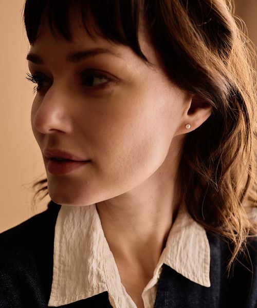 A close-up of a woman with short brown hair, wearing a white shirt and black blazer, looking to the side.