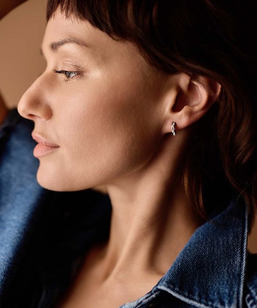 Close-up of a woman with short brown hair wearing earrings, side profile, wearing a blue denim jacket.