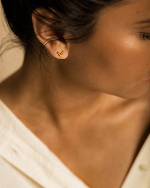 Close-up of a woman with gold earrings and smooth skin, wearing a white top. The photo focuses on her face and shoulder.