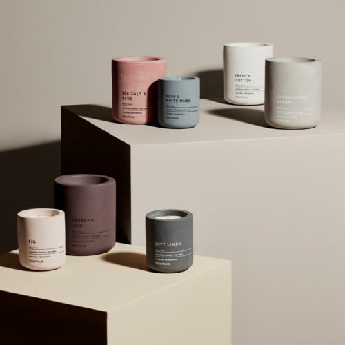 Six scented candles in pastel colors on different white blocks, with shadows and minimal background.
