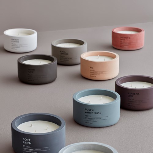 Colorful candles in round containers with simple labels are arranged on a flat surface.