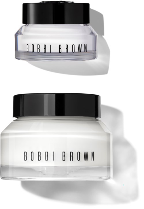 Två klara burkar med svarta lock märkta Bobbi Brown, solljus skapar skuggor på en vit yta.