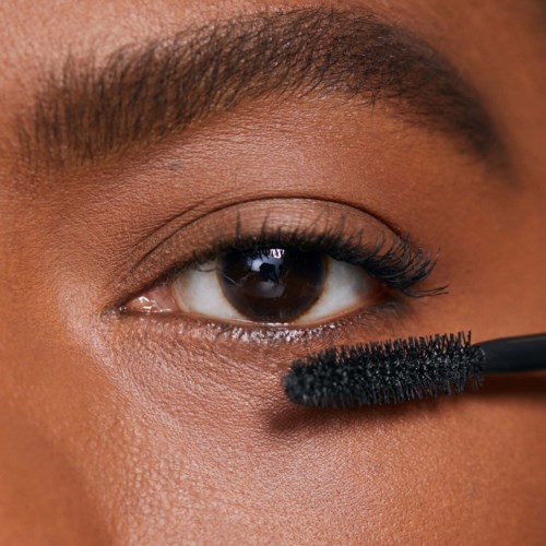 Eine Person trägt mit einer Bürste schwarzen Mascara auf die unteren Wimpern auf.