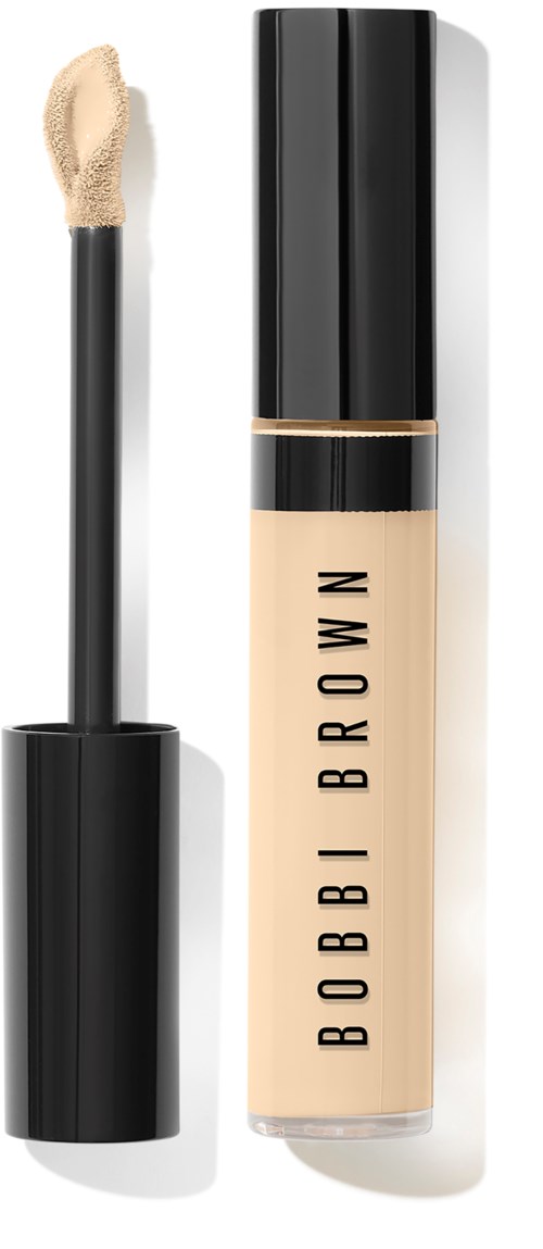 En Bobbi Brown flytande concealer-flaska med svart lock, tydligt rör som visar det beige produkten och en applikator.