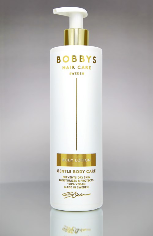 Een lang wit flesje met gouden pomp, gelabeld Bobby's Hair Care en Body Lotion, voor zachte huidverzorging.