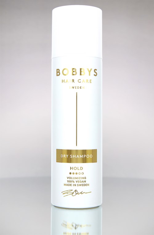 En vit flaska torrschampo märkt 'Bobby's Hair Care Sweden' med guld- och svart text och en minimal design.