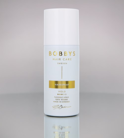 A white canister with gold and black text, labeled as Bobbys Hair Care Sweden Hairspray, standing on a plain background.