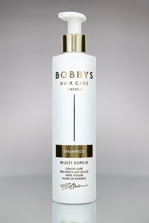 En vit schampoflaska med guld- och svarta accenter, märkt 'Bobby's Hair Care Sweden' och 'Multi Repair'.