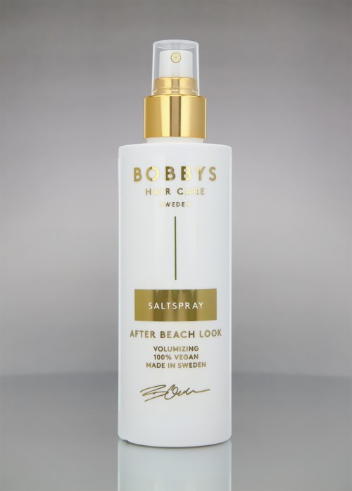 Een witte flesje van Bobbys haarverzorging zout spray met gouden accenten en pomp, bedoeld voor strandlook, veganistisch, gemaakt in Zweden.