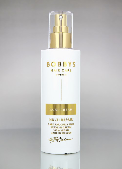 Witte fles met gouden en zwarte tekst, gelabeld 'Bobby's Hair Care', 'Curl Cream' en 'Multi Repair'.