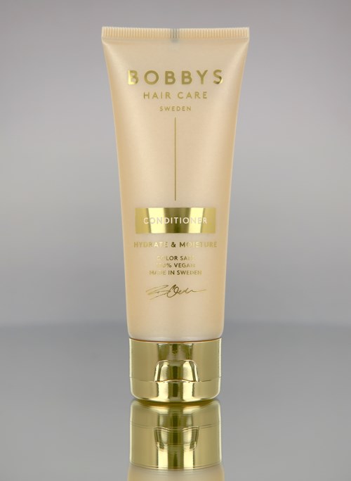 En beige och guldig tub med Bobby's Hair Care balsam, märkt för fukt och färgbehandling, med en enkel design.