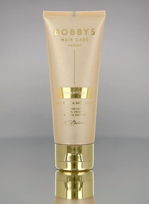 Bobby's Hair Care shampooputki, jossa kullan ja kermaiset värit, seisoo oikein päin heijastavalla pinnalla.