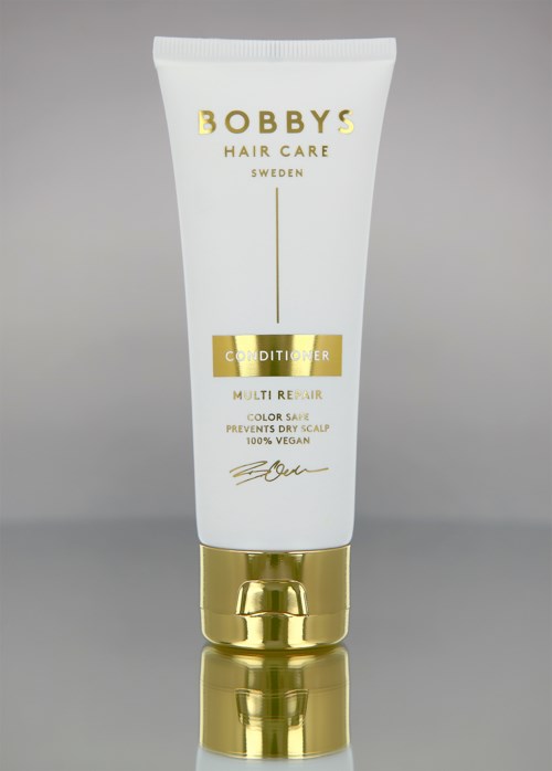 En vit tub med gulddetaljer, märkt 'Bobby's Hair Care Conditioner', står på en reflekterande yta.