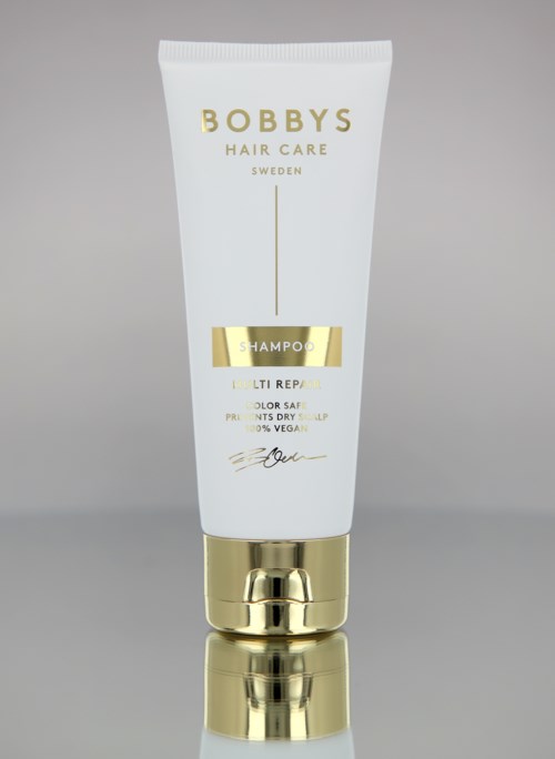 Een witte en gouden tube van BOBBY'S Hair Care shampoo met gouden dop op een grijze achtergrond.