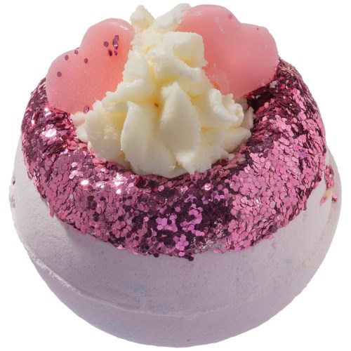 En rund badbomb med rosa glitter, vit kräm på toppen och rosa hjärtdekorationer.