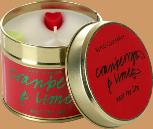 Et duftlys i métalæske med røde og pink etiketter, hjerteformet veke, og låg med teksten 'Cranberry & Lime'.