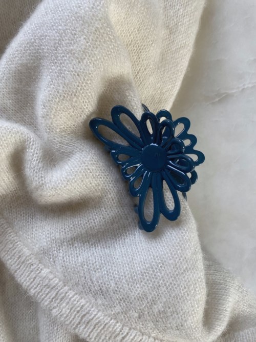 En blå blomformad hårklämma fäst vid mjukt, vitt tyg.