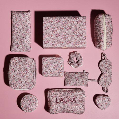 En samling med väskor och necessärer med blommönster i olika former och storlekar på en rosa bakgrund.