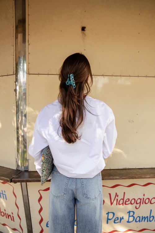 Ein Mädchen mit langen Haaren, blauer Haarspange, weißer Jacke und hellblauen Jeans steht mit dem Rücken zur Wand.