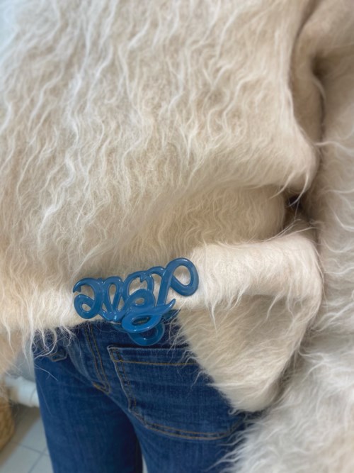 Ein flauschiger weißer Hund mit einem blauen Hundemarken an seinem Halsband, steht neben einer Person in blauer Jeans.