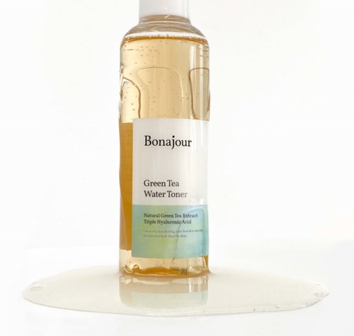 Läpinäkyvä pullo, jossa lukee "Bonjour Green Tea Water Toner" ja ympärillä vuotanut neste.