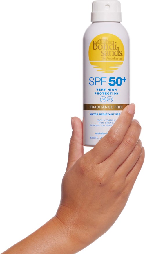 A hand holds a white bottle of sunscreen with SPF 50+, yellow and blue labeling, and a spray nozzle.