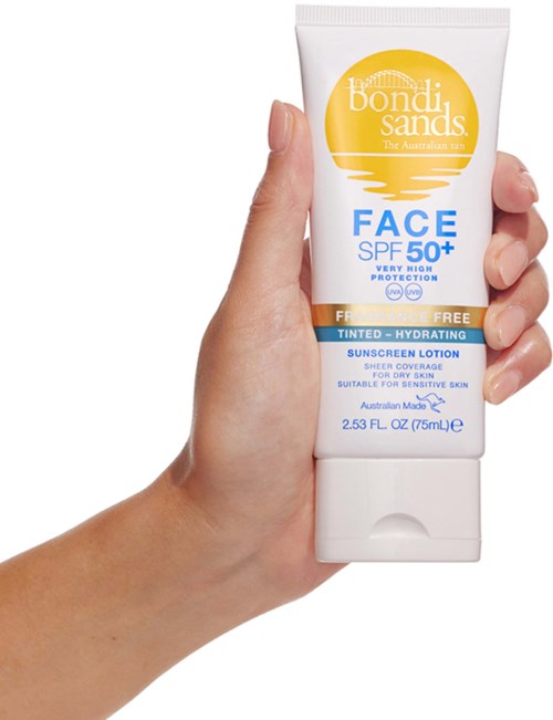 A hand holding a white tube of sunscreen with yellow, blue, and white label, showing SPF 50+ protection.
