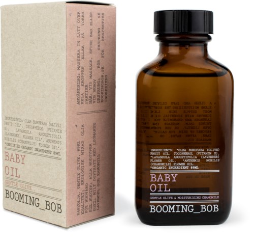 En liten mörk glasflaska märkt 'Baby Oil' bredvid en ljus låda, båda innehållande olivolja och kamomill.