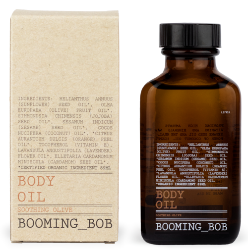 Brązowa butelka z napisem 'Body Oil' i etykietą 'Soothing Olive' obok beżowe opakowanie z listą składników.