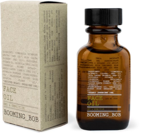 Mała brązowa butelka z napisem 'FACE OIL' i 'BOOMING_BOB' obok beżowego pudełka z tekstem i instrukcjami.