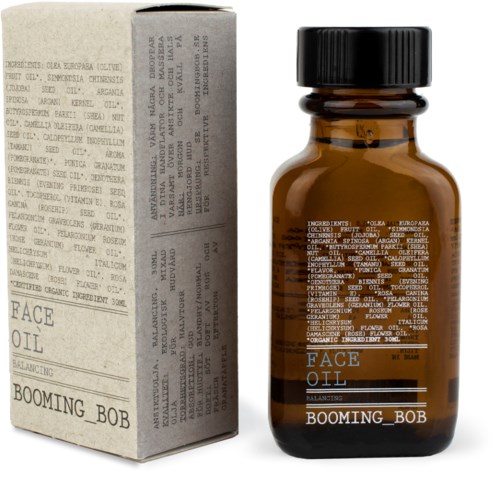 En liten brunt flaska med svart lock och en matchande låda med liten text, märkt "Face Oil" och "Booming Bob."