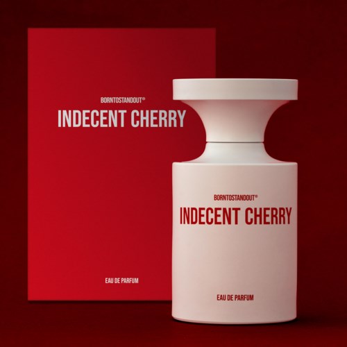 Valkoinen hajuvesipullo, jossa lukee "Indecent Cherry", ja punainen laatikko samalla tekstillä, tummanpunaisella taustalla.