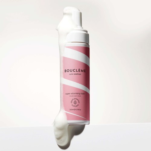 En pink og hvid flaske af Bouclème super volumising skum med en buet design og hvidt låg.