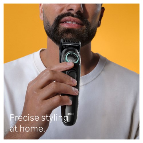 Ein Mann mit Bart hält einen Haarschneider in der Nähe seines Gesichts vor einem gelben Hintergrund. Der Text lautet 'Precise styling at home.'