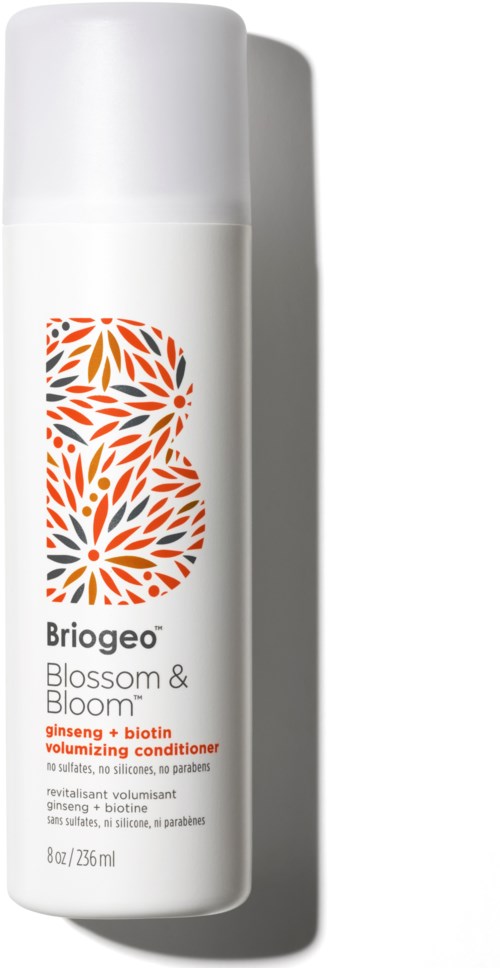 En hvit flaske med oransje og rød blomsterdesign. Det er en volumiserende balsam med ginseng og biotin.