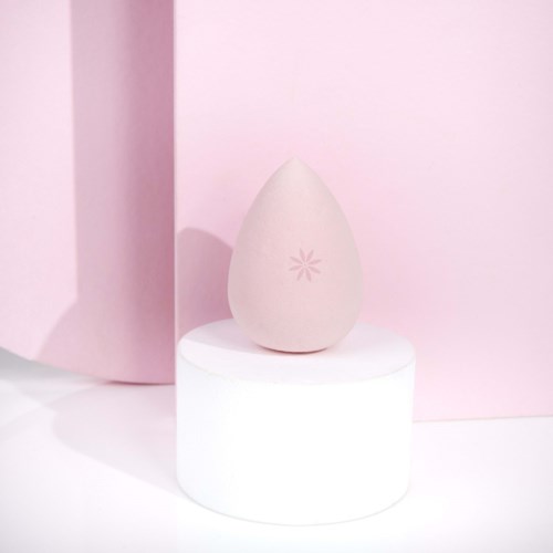 Een beige make-up spons met een roze sneeuwvlok-achtig ontwerp, op een witte ronde standaard.