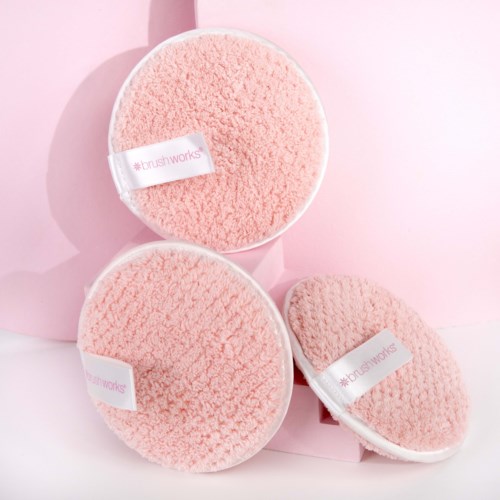 Drie pluizige roze schoonmaakschrobbers met labels, tegen een roze achtergrond.
