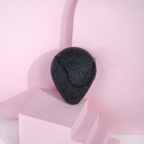 En svart, strukturert stein formet som en dråpe, plassert på rosa trappetrinn med rosa bakgrunn.