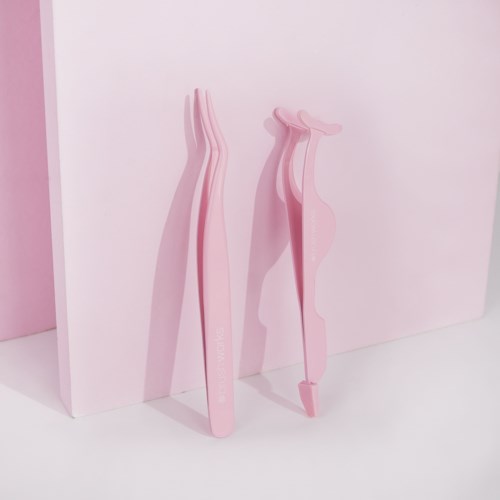 Pink eyelash curlers with a handle and a curved top, placed on a pink background.
