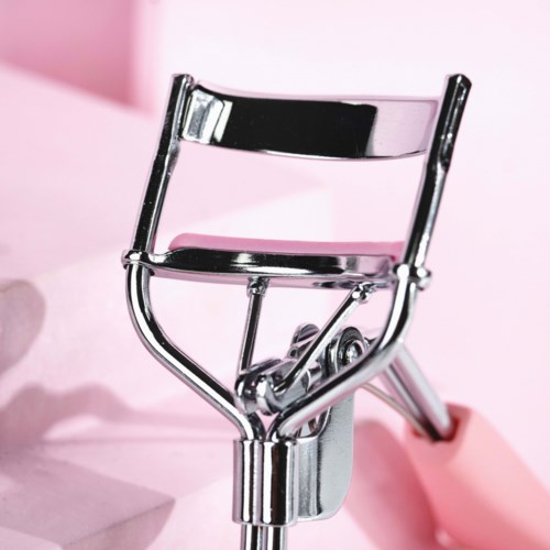 A metal eyelash curler on a pink background.