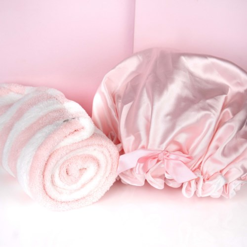 Rosa och vit randig handduk och glansig rosa satinmössa på en rosa bakgrund.