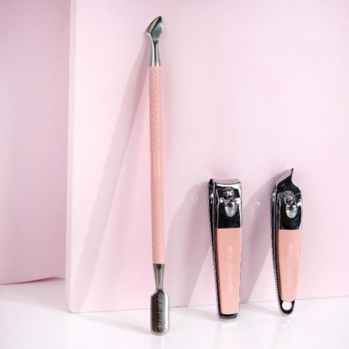 Drie schoonheidsgereedschappen met roze handvatten, twee zijn nagelknippers, en een is een klein schuin gereedschap, allemaal op een roze achtergrond.