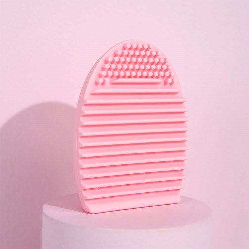 En lyserød silikonebørste med tekstureret side, oval form, på en hvid pedestal, med lys pink baggrund.