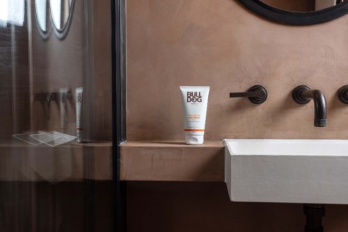 Ein Badezimmer mit Waschbecken, schwarzer Wasserhahn und einer Flasche mit "BULLDOG"-Aufschrift auf der beigen Ablage.