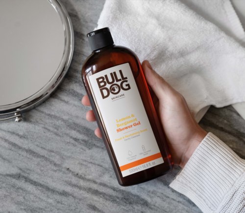 Ruskea pullo Bulldog Skincare Lemon & Bergamot Shower Gel ja peili ja valkoinen pyyhe.