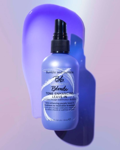 En lila flaska med svart spraylock, märkt Bumble and Bumble Blonde Leave-In behandling, mot en lila bakgrund.