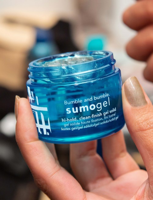 A person holds an open blue jar of gel, labeled "SUMOGEL," with a finger touching the gel surface.