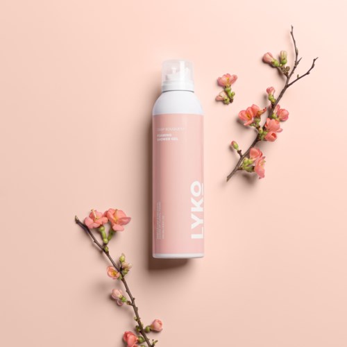 En rosa och vit flaska omgiven av rosa blommande grenar på rosa bakgrund.