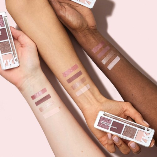 Tre arme med forskellige hudtoner viser swatches af lyserødt, brunt og hvidt makeup og makeup paletter.